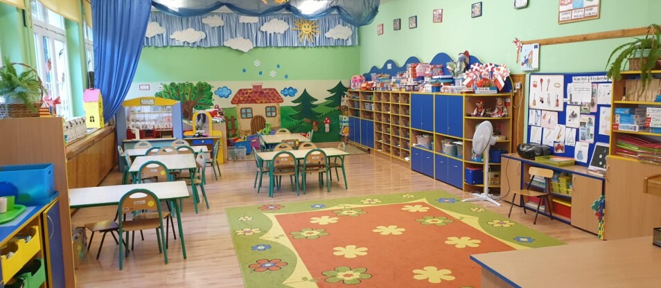 Sala oddziału szóstego. Przy wejściu znajduje się kolorowy dywan. W centralnej części stoją stoliki i krzesełka. Po prawej stronie ustawione są meble z pomocami dydaktycznymi i zabawkami dla dzieci. Na końcu sali stoją meble , pudełka z zabawkami oraz kąciki tematyczne.