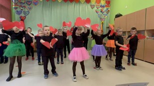 Dzieci w kolorowych strojach występujące przed publicznością, trzymające w dłoniach serca z papieru